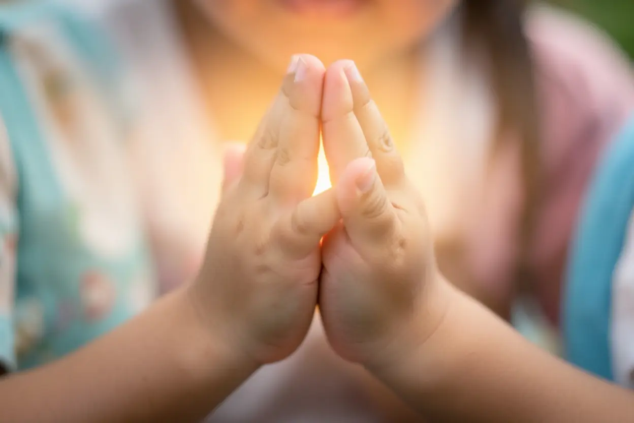 Mãos de criança em oração, simbolizando o resumo dos ensinamentos e a prática da fé.