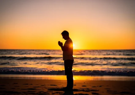 Batismo: Como Viver a Nova Vida em Cristo após Descer às Águas Pessoa orando ao nascer do sol representando a nova vida cristã após o batismo.